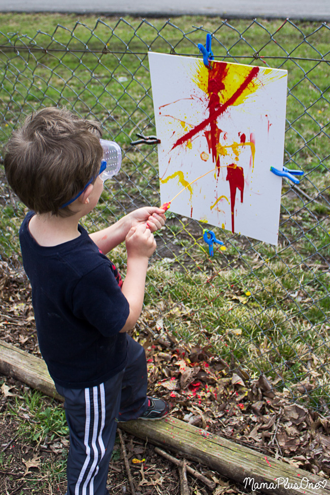 Kids bored this summer? Let them be kids with this awesome messy play activity! This splatter painting uses water balloons, medicine droppers, squirt guns, and more to create a unique piece of abstract art your kids will love creating. Don't worry-- kids and clothes are both washable! #allEssentials